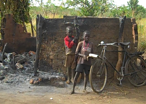 The children stand in front of their burnt out house